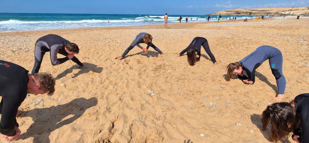 Beginners warming up on the beach before their first surf lesson — Discover week