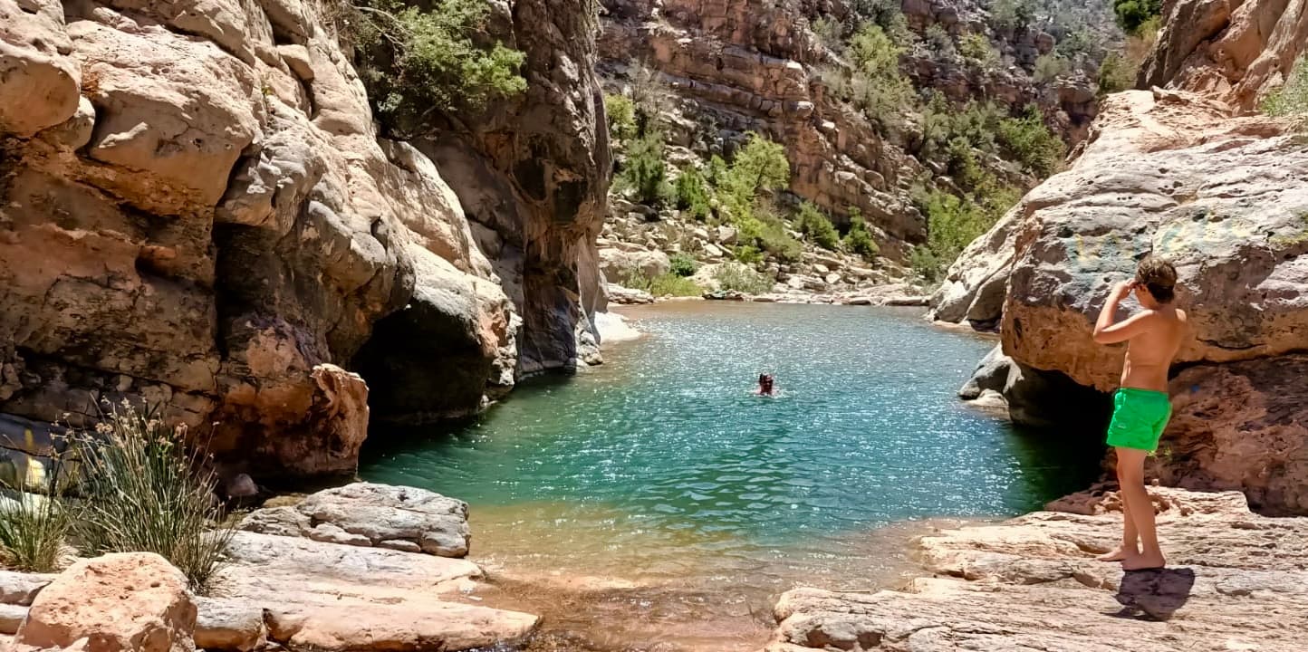 Turquoise natural pool between red rock canyon walls with swimmers