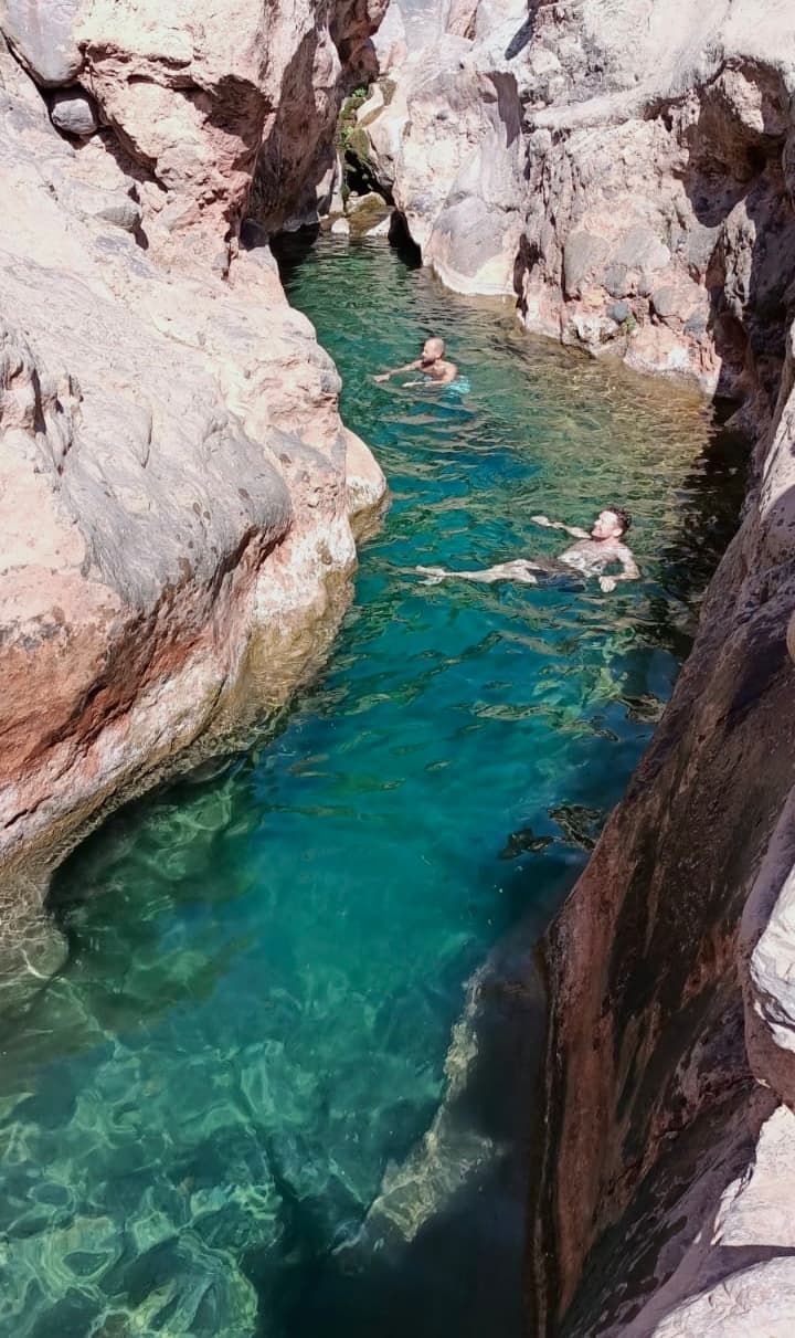 Narrow turquoise pool between dark canyon walls with swimmers